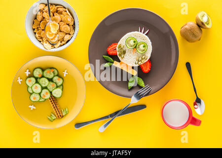 Divertente colorato la prima colazione per i bambini in forma di gufo e albero con cornflakes, kiwi e latte isolate su giallo Foto Stock