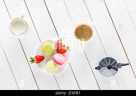 Vista dall'alto di macarons con caffè e fragole sul piano portapaziente in legno Foto Stock