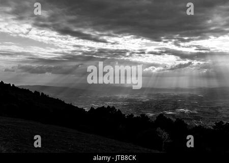 Vista di una valle da una montagna, con raggi di sole che fuoriesce attraverso le nuvole e illuminazione di alcune zone del terreno Foto Stock