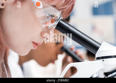 Vista laterale di professionale di giovani ricercatori che operano con microscopi in laboratorio chimico Foto Stock