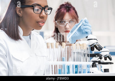 Professionale di giovani ricercatori che operano con microscopio e provette per la prova in laboratorio chimico Foto Stock