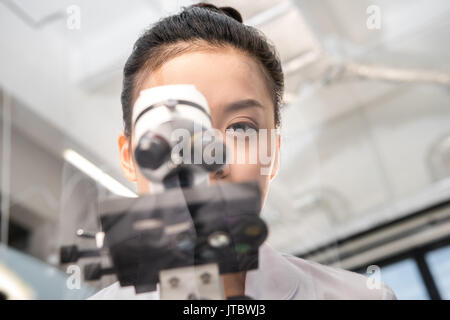 Vista parziale di scienziata guardando attraverso il microscopio su reagenti in laboratorio Foto Stock