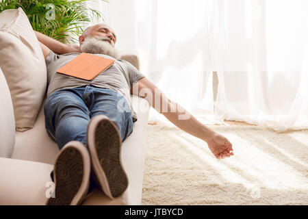 Senior uomo barbuto che dorme sul divano con tavoletta digitale in casa Foto Stock