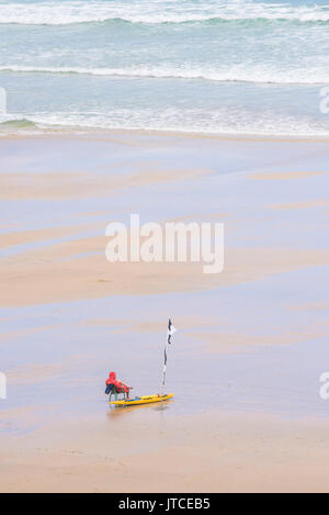 Un lone RNLI bagnino di turno su una tranquilla spiaggia deserta in Newquay, Cornwall. Foto Stock