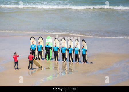 Un gruppo di scuole di surf gli studenti in posa per una fotografia di Great Western Beach in Newquay, Cornwall. Foto Stock