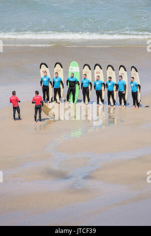 Un gruppo di scuole di surf gli studenti e i loro insegnanti su Great Western Beach in Newquay, Cornwall. Foto Stock