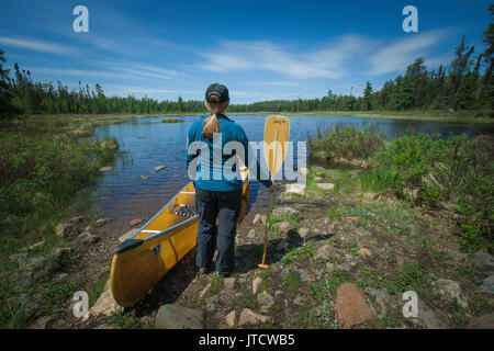 Una femmina paddler portages la sua canoa attraverso un sentiero in acque di confine canoa Area Wilderness (BWCAW). Foto Stock