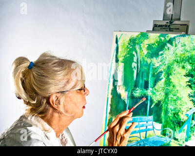 Bionda, pony-tailed senior professional artista lavora su una tela sulla base di una fotografia ha preso a Giverny, in Francia, presso la tenuta di Claude Monet. (Ar Foto Stock