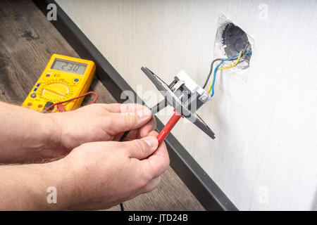 Elettricista in una presa a muro con multimetro elettronico Foto Stock