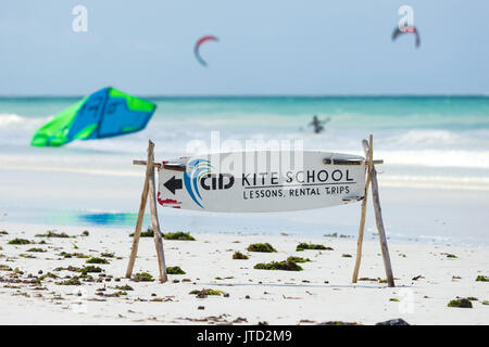 Scuola di Kite segno sulla spiaggia con kitesurfisti nell'oceano sullo sfondo, Diani, Kenya Foto Stock