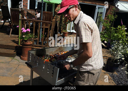 L'uomo la cottura a un barbecue in giardino durante i mesi estivi Birmingham West Midlands England Foto Stock