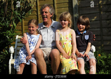 Nonno con i nipoti seduta sul banco sorridente in giardino nei mesi estivi Birmingham West Midlands England Foto Stock