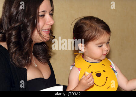 Ragazza seduta sulle madri giro in plastica da indossare Winnie The Pooh bib mentre mangia pane Inghilterra Foto Stock