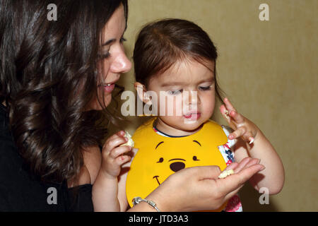 Ragazza seduta sulle madri giro in plastica da indossare Winnie The Pooh bib mentre mangia pane Inghilterra Foto Stock