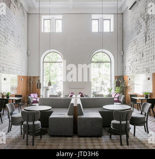 Cafe in stile loft con squallide pareti di luce strutturata con pannelli di legno e un pavimento piastrellato. Ci sono divani multicolore, diversi tavoli e sedie, Foto Stock