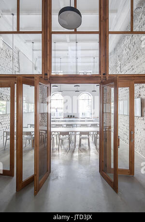 Cafe con squallide pareti chiare e una grande partizione in legno con finestre e porte di vetro. Vi sono ampi tavoli bianchi con sedie, finestre ad arco, appeso Foto Stock