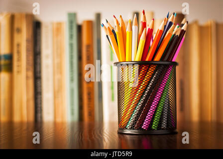 Filo portapenna pieno di matite colorate in piedi su un tavolo in legno nella parte anteriore di una libreria piena di libri con shallow dof e copyspace Foto Stock