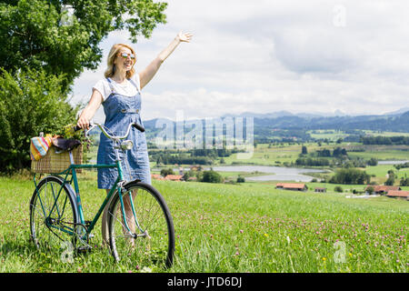 Donna che cammina con retro bicicletta. sventolando con il braccio sollevato. Foto Stock