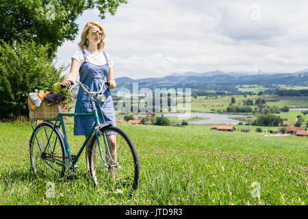 Donna che cammina con bicicletta retrò e cestello sul prato di fiori Foto Stock