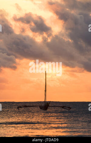 Barca Dhow stagliano in inizio di mattina di rottura alla luce del sole attraverso le nuvole oltre oceano Indiano, Diani, Kenya