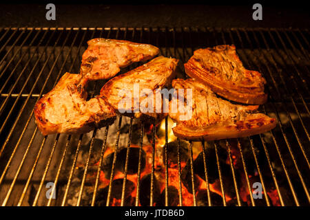 Costolette di maiale con osso, marinato nel succo di limone, sfrigolante su un open-fuoco barbecue a carbone, quasi pronto da mangiare Foto Stock