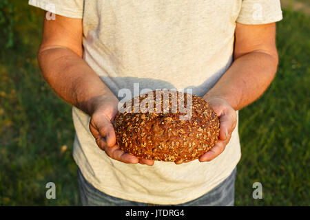 Baker uomo azienda biologica rustica pagnotta di pane in mani. Luce naturale. Foto Stock