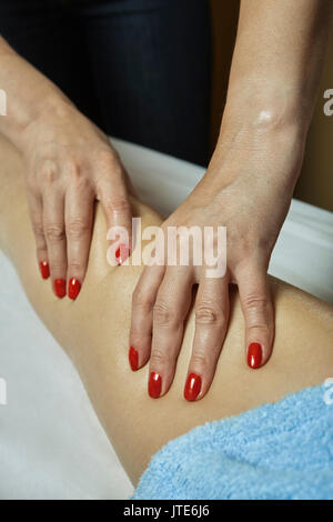 Dettaglio con le mani della massaggiatrice professionale applicando pressione massaggio sul ginocchio e coscia del paziente di sesso femminile in terapia salon. stress i muscoli rilasciare proc Foto Stock