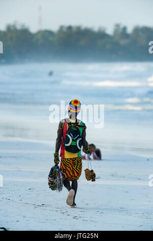 Uomo locale passeggiate lungo la spiaggia con prodotti per la vendita in tarda serata luce, Diani, Kenya Foto Stock