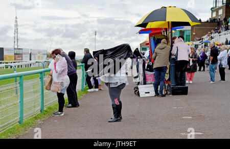 Brighton, Regno Unito. Il 9 agosto, 2017. Questo racegoer ha problemi con la casacca nel vento e pioggia a Marstons il giorno della gara in Maronthonbet festival di corse a Brighton Racecourse Credito: Simon Dack/Alamy Live News Foto Stock