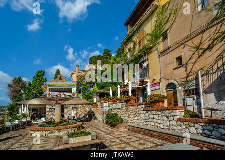 Piccolo quadrato a Taormina Italia sull'isola di Sicilia con un ristorante e un appartamento con una donna a stirare sul balcone Foto Stock