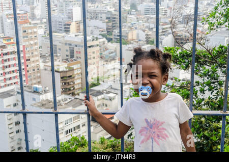 Una ragazza (4-6) sorrisi con Ipanema, a Rio de Janeiro sullo sfondo. Un messaggio scritto su una ragazza del braccio che si traduce in "mi manchi mamma". Prese a Cantagalo Foto Stock