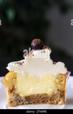 Il tiramisù cupcake su una piastra con una forchetta. Sul tavolo. Cioccolatini e rabboccato.; angel food cupcake e crema di mascarpone. Sfondo scuro. Nel taglio. Foto Stock