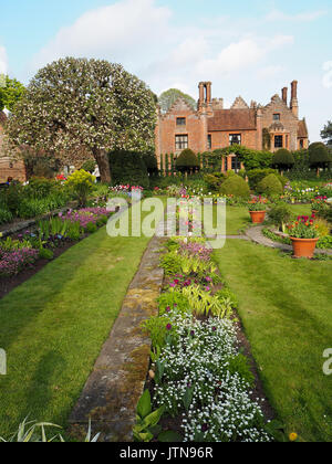 Visualizzazione verticale di Chenies Manor e affondata giardino in primavera con percorsi di erba, tulipani e albero della mela in bel tempo. Foto Stock