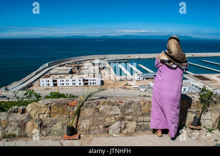 Nord Africa: una donna musulmana di fronte al porto di Tangeri guardando lo Stretto di Gibilterra che separa il Marocco dalla Spagna Foto Stock