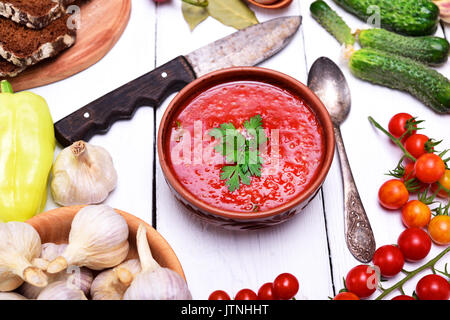 Zuppa di verdure fresche gazpacho in ceramica piastra marrone su un tavolo bianco, intorno gli ingredienti per cucinare su una prescrizione Foto Stock