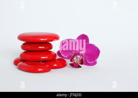 Red ciottoli disposti in stile zen con un rosa scuro orchid sul lato destro su sfondo bianco Foto Stock