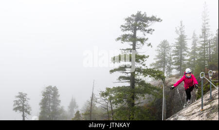 Una donna attraversa un piccolo ponte di sospensione che è parte della Via Ferrata in Squamish, British Columbia. Foto Stock