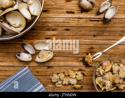 Foto aerea di cotto a vapore poco collo essendo di vongole sgusciate sul bordo di taglio. Asciugamani blu, svuotare i serbatoi Clam Clam e la carne può essere visto nella foto. Foto Stock