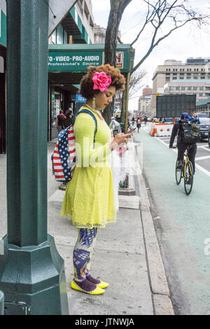 Deliziosa giovane fashionista indossando faux rose nel suo afro, un daffodil maglione colorato mantello & Scarpe, Stars & Stripes zaino, wild collant stampati Foto Stock