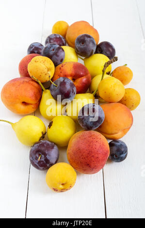 Un mucchio di succosa frutta estiva in bianco sullo sfondo di legno (prugne, albicocche, pere). Il raccolto dal giardino. Una fonte naturale di vitamine. Foto Stock