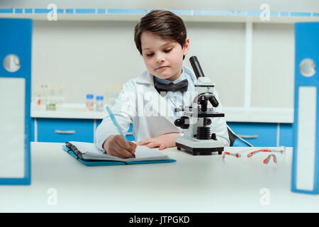 Scolaro con microscopio e copybook in Science Laboratory, Laboratorio di scienze concetto per bambini Foto Stock