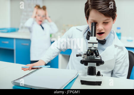 Scolaro con microscopio e copybook in Science Laboratory, Laboratorio di scienze concetto per bambini Foto Stock