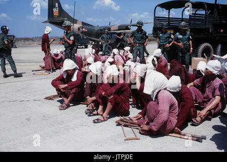 Il Viet Cong POWs sedersi sulla rampa a Tan Son Nhut Air Base sotto lo sguardo vigile del Vietnam del Sud della polizia militare. I prigionieri di guerra sono stati portati alla base aerea in 6x6 camion in background e sarà trasferito in aereo a Loc Ninh, Sud Vietnam sul C-123 di aerei da trasporto per la scambio di prigionieri tra gli Stati Uniti/Vietnam del Sud e Vietnam del Nord/Viet Cong forze armate. Foto Stock