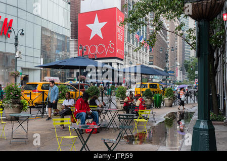 I Newyorkesi sedersi sotto gli ombrelloni in Herald Square nel centro cittadino ad aspettare la pioggia. Solo uso editoriale Foto Stock