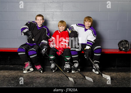 Tre ragazzi giovani giocatori di hockey pongono in spogliatoio nel loro equipaggiamento Foto Stock