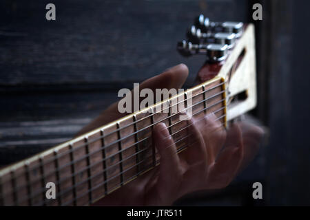 Dita suonare la chitarra acustica su nero scuro dello sfondo in legno con il fuoco selettivo e la sfocatura in movimento Foto Stock