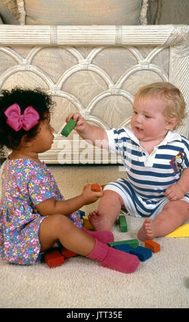 Giovani caucasici condivisione bambino dà il blocco del giocattolo di African American 2 anno vecchia ragazza 18 mese old boy © Myrleen Pearson Foto Stock