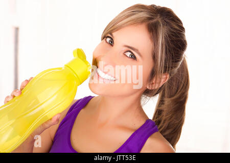 Bella donna sorridente indossare una t-shirt viola e di bere una bottiglia di colore giallo di acqua Foto Stock