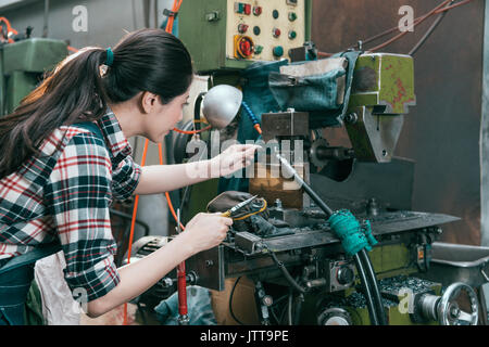 Vista posteriore foto di eleganti donna tornio lavoratore lavorando a macchina fresatrice dipartimento e utilizzando le pinze strumento componenti di regolazione. Foto Stock