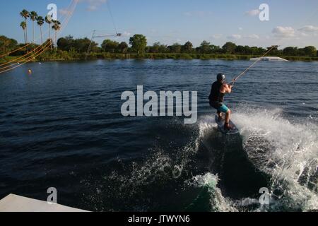 Giovane donna di essere lanciato tirato dal cavo sul Wakeboard nel lago Foto Stock